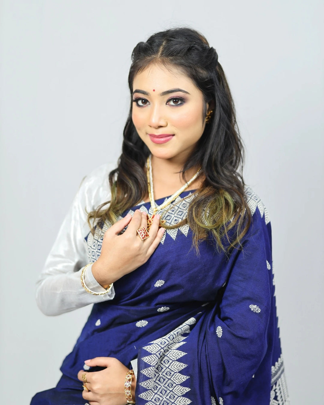 Woman wearing a blue mekhela sador with white patterns on a plain background