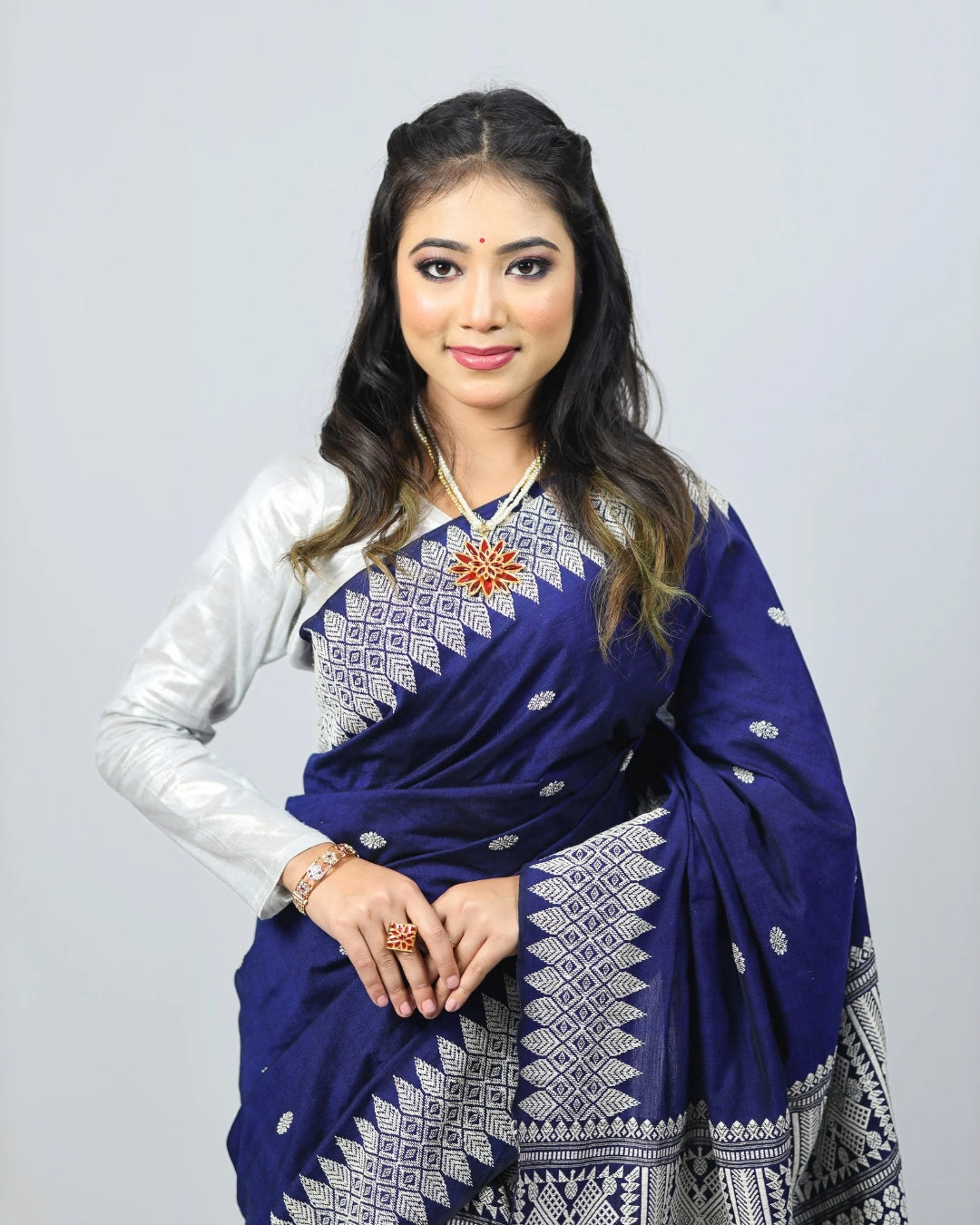 Woman wearing a blue mekhela sador with white patterns on a plain background