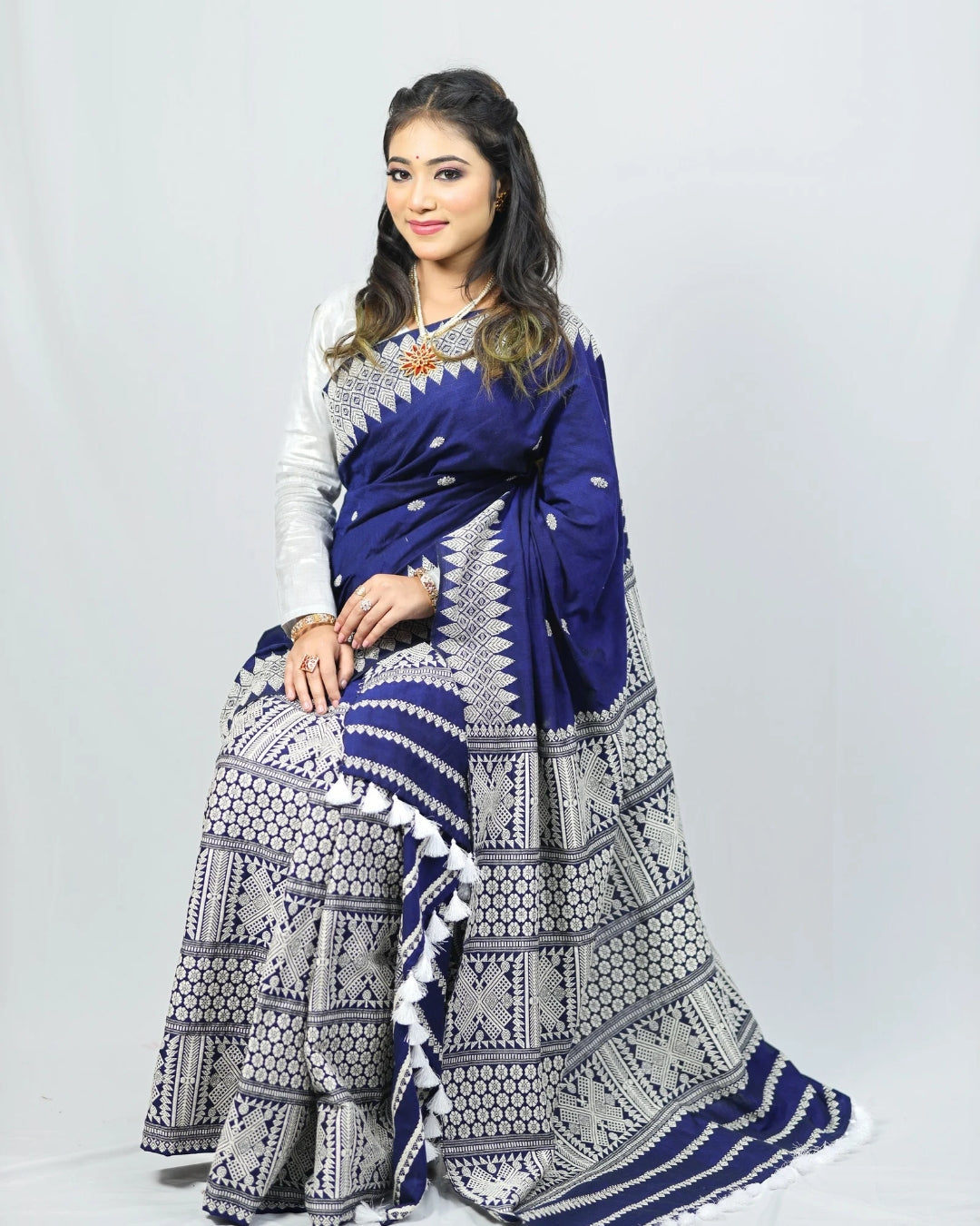 Woman wearing a blue mekhela sador with white patterns on a plain background