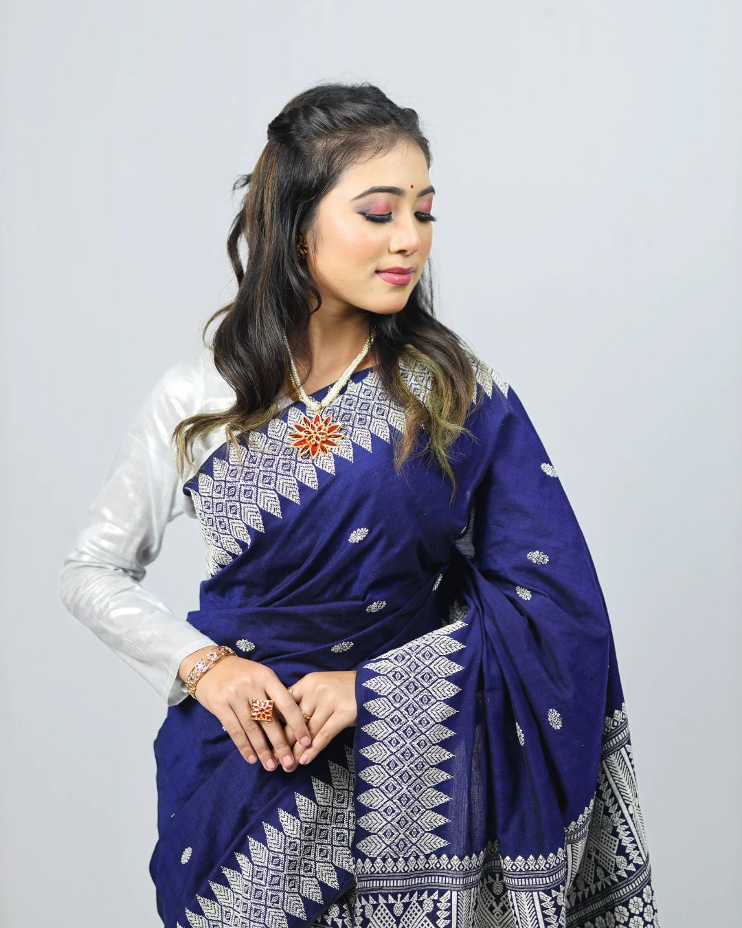 Woman wearing a blue mekhela sador with white patterns on a plain background